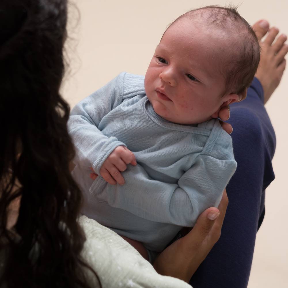 A baby being held wearing a Sleep Store Deluxe New Zealand Merino Wool Long Sleeve Bodysuit in the colour Soft Sky.