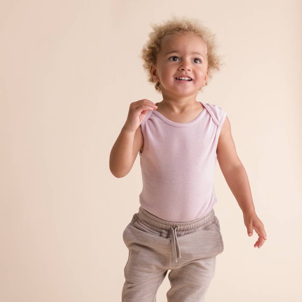 A young girl standing wearing a Sleep Store Deluxe New Zealand Merino Wool Singletsuit in Blush paired with Oat pants.