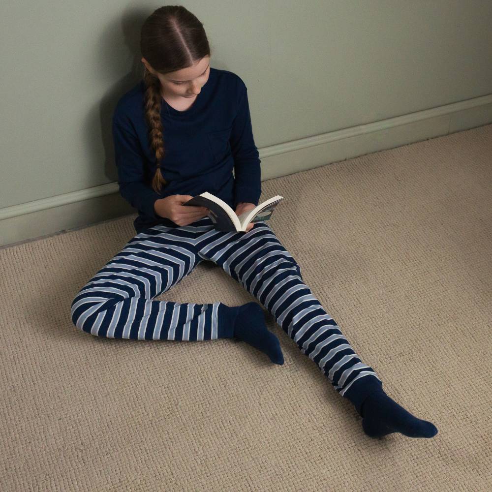 A girl sitting on the floor reading a book wearing the Woolbabe Merino/Organic Cotton Relaxed Winter Pyjamas in the colour Midnight/Glacier.