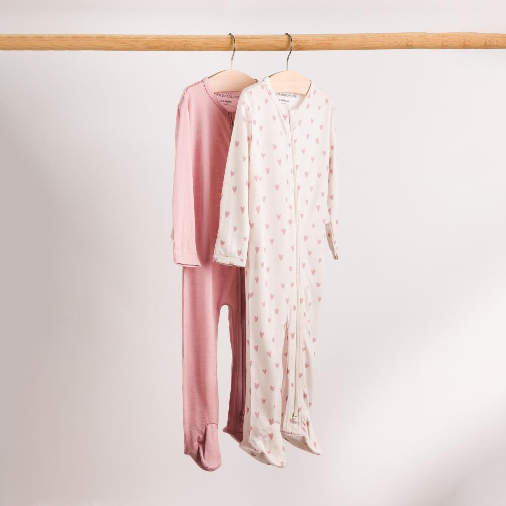 A hanging shot of 2 Sleep Store All Seasons Merino/Tencel Footed Zipsuits on a wooden rail.