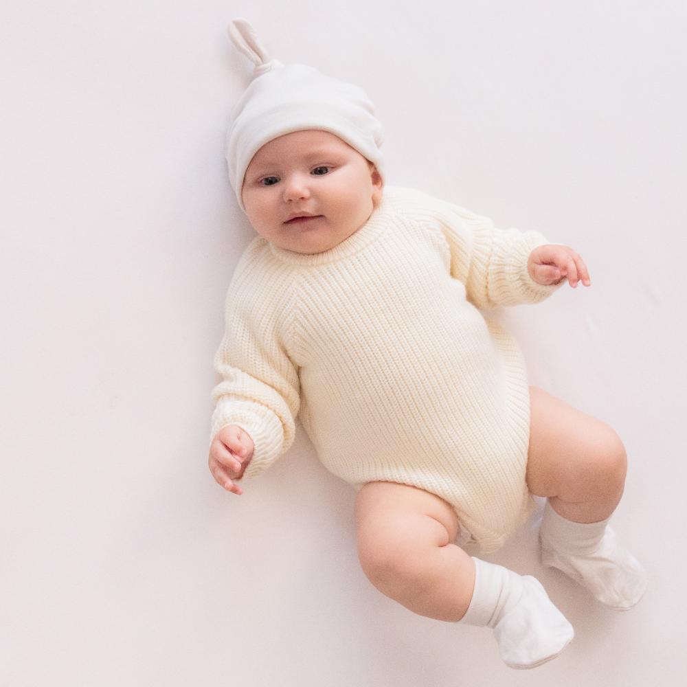 A baby lying down wearing a Cream colour Sleep Store Merino Knitwear Bubblesuit.