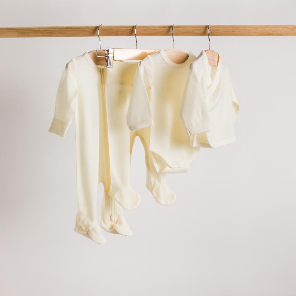 NZ Jersey Merino footed onesie, footed pants, kimono cardigan and long sleeve bodysuit in cream hanging on a rack