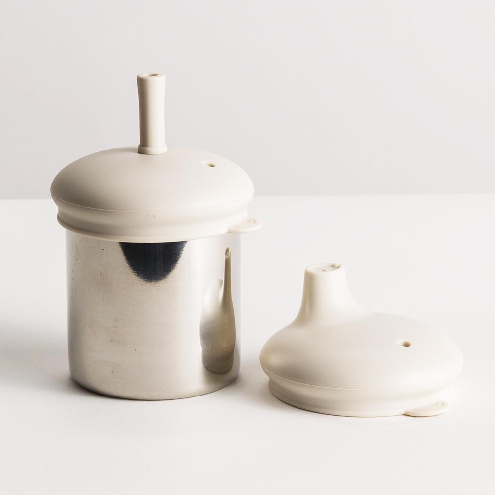 The Nestling Stainless Insulated Sip & Straw Cup in the Oat colour. The cup has the straw lid and straw attached with the sipper lid on it's own next to it.