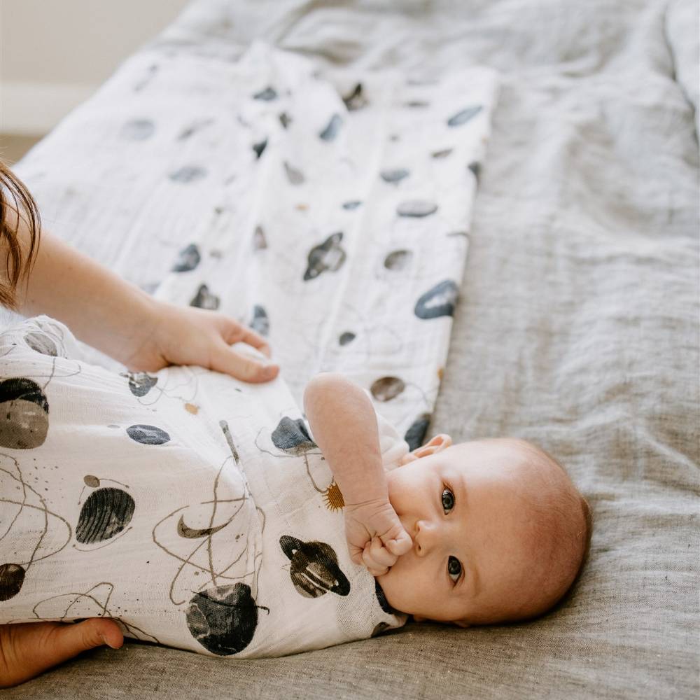 mum swaddling baby on bed in the 100% cotton muslin swaddle by Little Unicorn