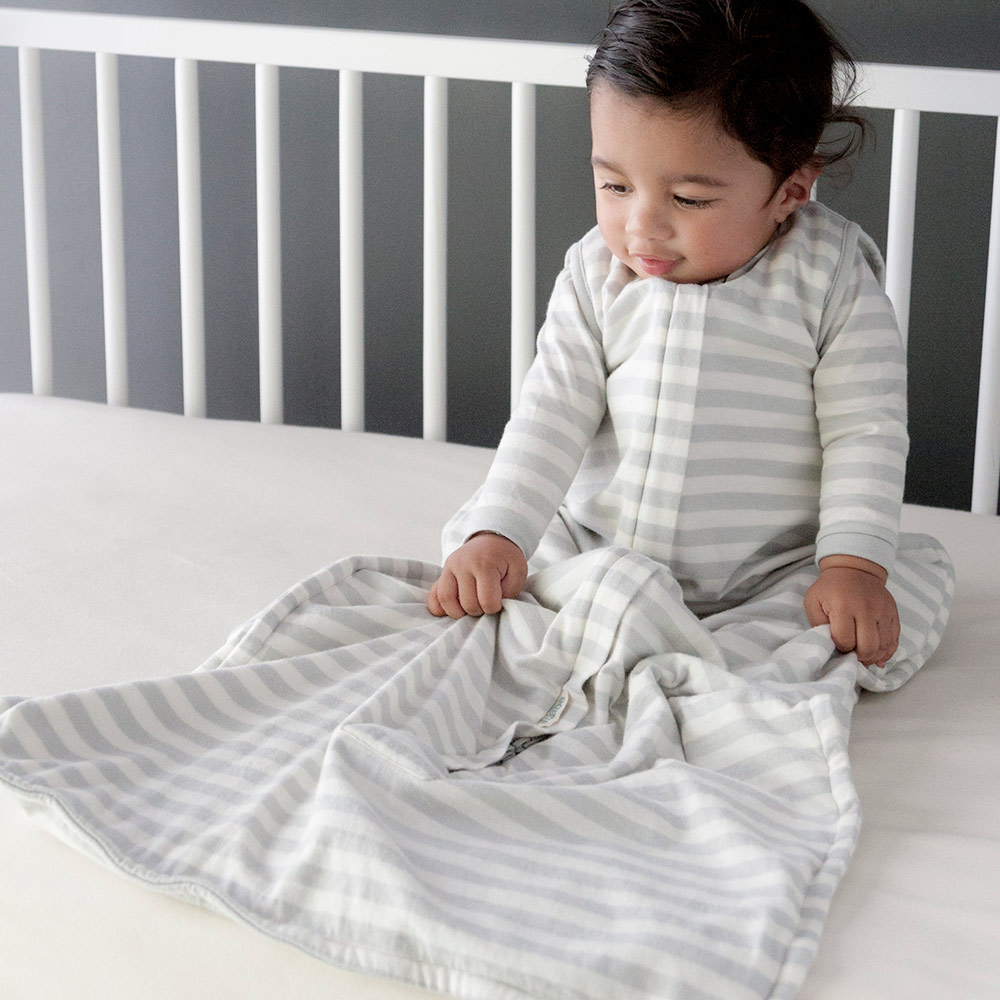 Baby sitting in cot wearing the Woolbabe Summer Sleeping Bag in pebble