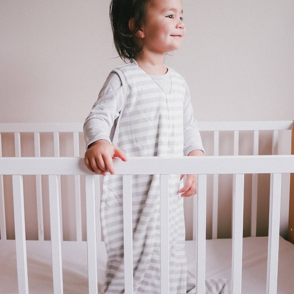 toddler standing in cot wearing woolbabe 3 seasons sleeping bag