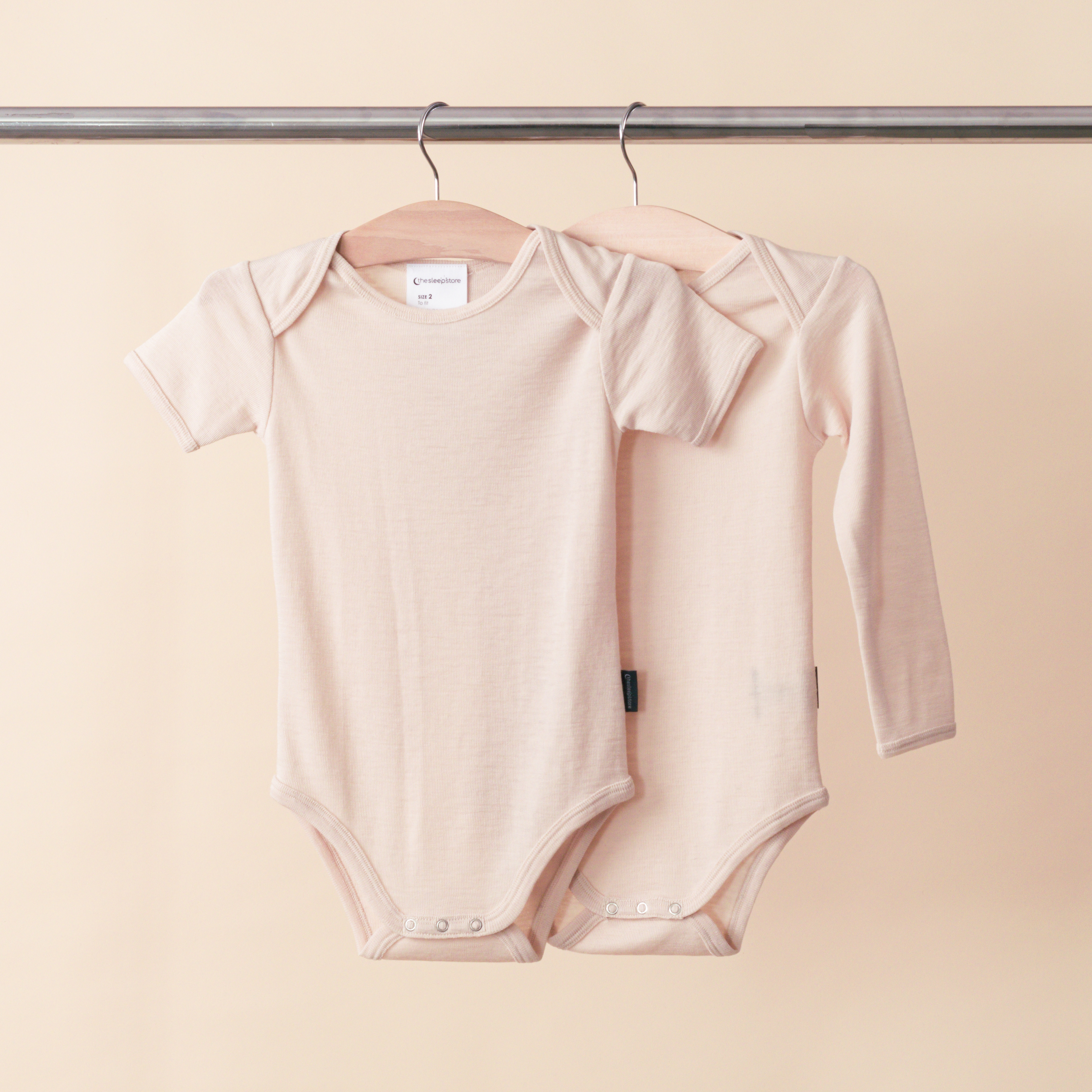 Deluxe Merino Rib Short-Sleeve and Long Sleeve Bodysuits hanging on a rail.