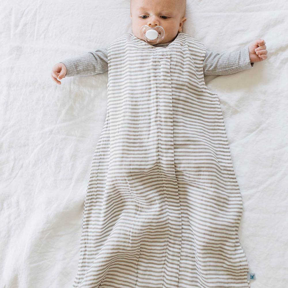 Baby with dummy lying in cot wearing the 1.0 tog rated 100% cotton muslin sleeping bag in grey stripe