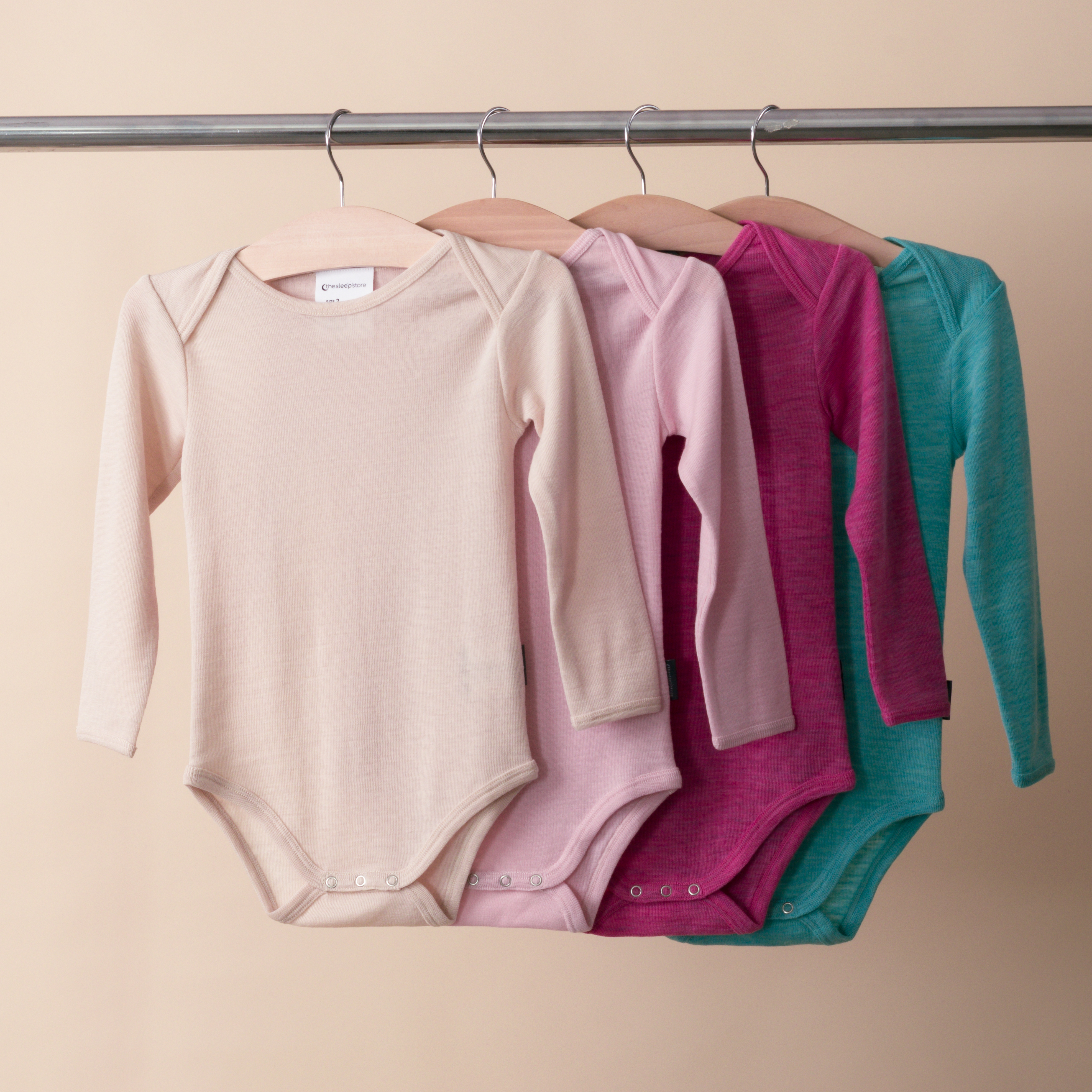 Row of The Sleep Store Deluxe Merino Rib Long Sleeve Bodysuit's hanging on a rack. 2024 season colours including Lollipop and Lagoon at the back of the rack