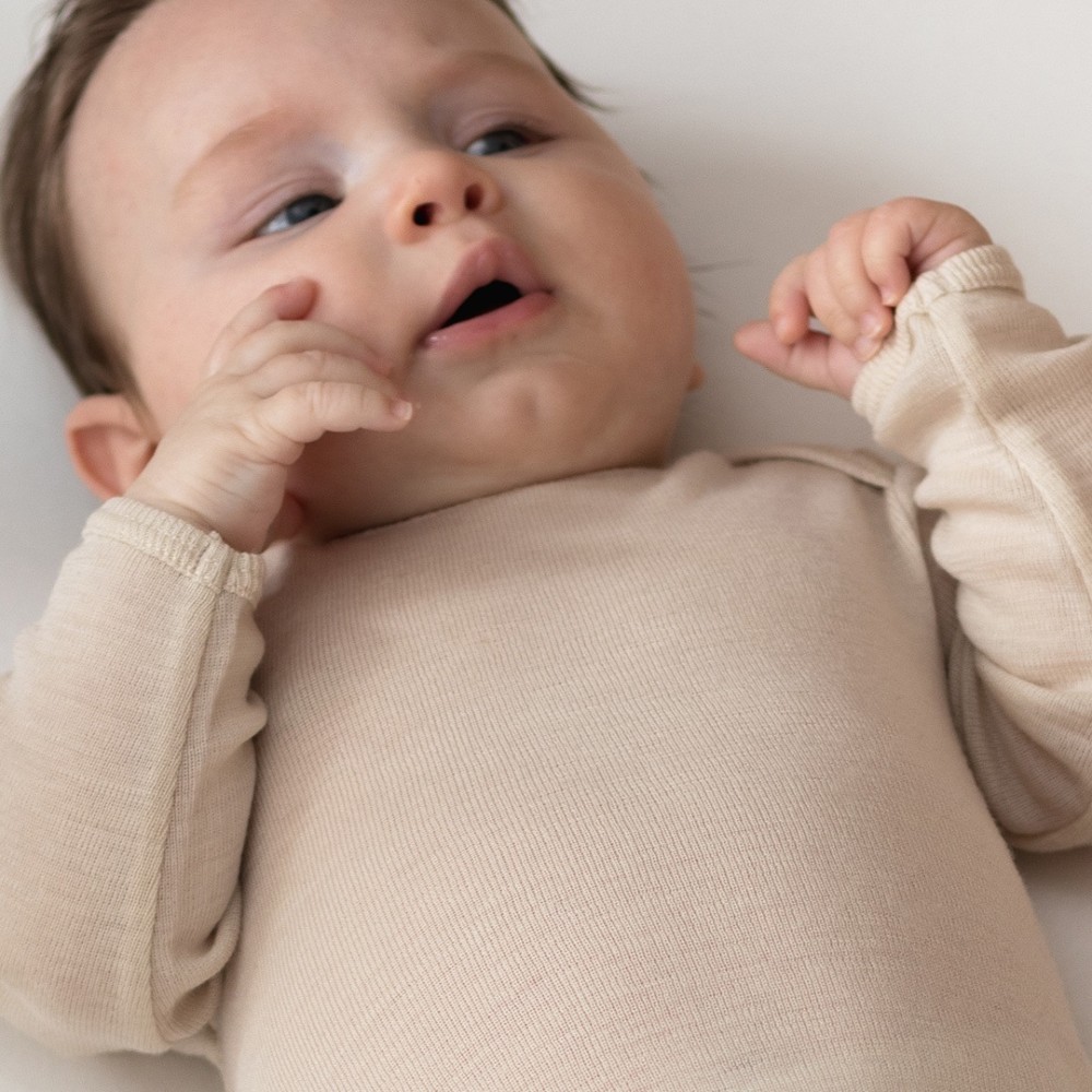 close up of 4 month old baby wearing The Sleep Store Deluxe Merino Rib Long Sleeve Bodysuit in Almond