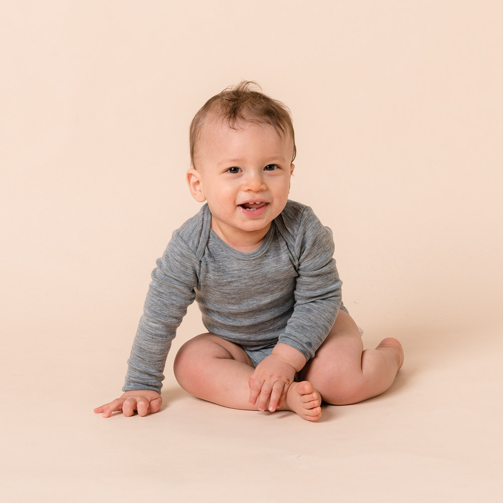 Baby sitting up wearing The Sleep Store Deluxe Merino Rib Long Sleeve Bodysuit in Grey