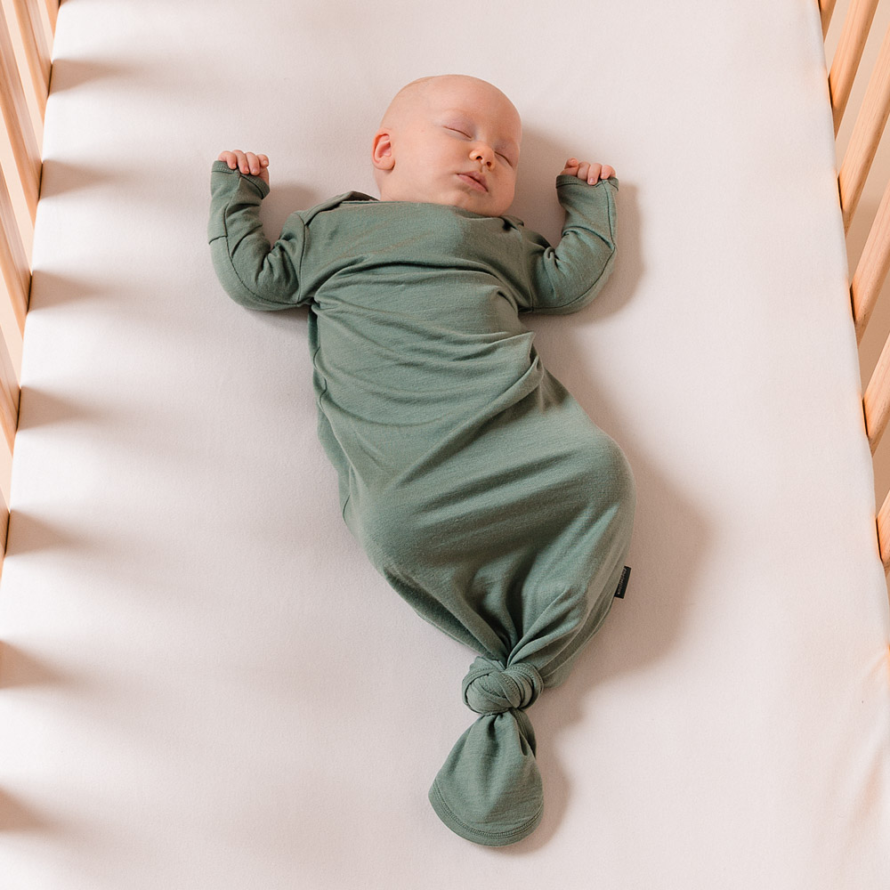 Newborn baby asleep in cot wearing jersey merino knotted gown in sage
