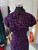 Close-up of royal purple qipao bodice showing traditional Chinese frog button, teardrop keyhole and all-over gold and pink glitter bead appliqué detail