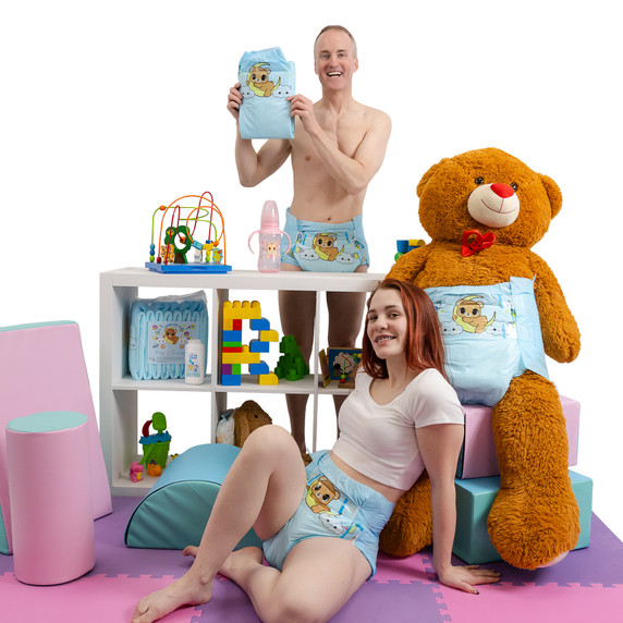 Male model standing behind shelf wearing and holding a Lunar Cub diaper, female model wearing Lunar Cub sitting in front of shelf and giant teddy bear, that is also wearing Lunar Cub.