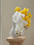 White and yellow Artificial phalaenopsis orchid flowers in a white vase on a wooden stand decor.