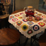 Handmade crochet daisy tablecloth with colorful flowers and white background on a wooden table setting.