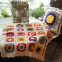 Handmade crochet daisy blanket with multicolored flowers on a table with decorative pillow and lantern.