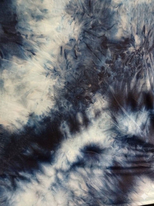 A close-up photograph of a piece of tie-dye fabric featuring irregular, organic patterns. The colors are predominantly deep navy and indigo blues blended with areas of ice-white and very pale blue, creating a mottled, almost cloudy effect with dark, spiky dye blotches and softer, fanned-out bleeds. The fabric is slightly creased and folded, showing its soft, slightly plush texture