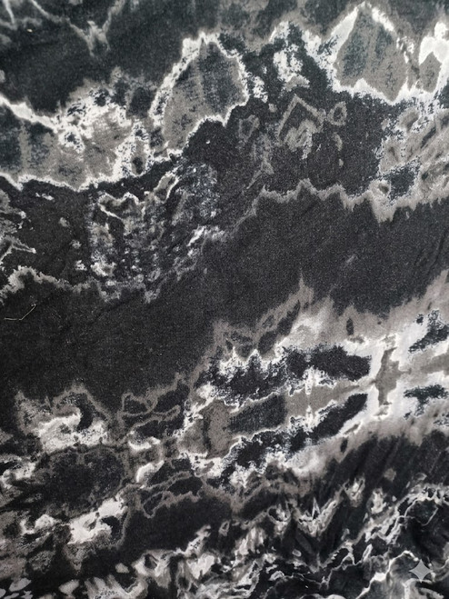Close-up of a textile featuring a monochromatic abstract marble or topographical pattern in shades of charcoal black, slate gray, and crisp white. The fabric shows a fine knit texture with flowing, organic wave-like designs reminiscent of tie-dye or natural stone veining