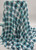 A high-resolution product photograph of Teal and Black Distressed Plaid Chiffon fabric, made of 100% polyester. The fabric features a weathered, abstract plaid pattern in vibrant teal and deep black over a white base.