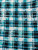 A top-down, flat lay photograph of a textile pattern. The fabric features a bold, grid-like plaid design composed of deep teal, turquoise, and black lines against a white background. The pattern has a distressed, textured appearance, with the lines showing speckled and broken effects, resembling worn paint or a hand-printed look.