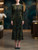 Full-length direct front pose, wearing a long-sleeve, fitted midi cocktail dress made from Midnight Olive Gold & Deep Teal Geometric Devoré Stretch Velvet Burnout Fabric. The intricate geometric pattern covers the entire dress, which has a high neck and flared hem.