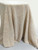 Cream-colored sherpa fleece fabric draped over a surface against a clean, neutral white background, highlighting the thick, pebbled texture and soft pile.