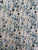 Close-up flat lay of 100% rayon challis dress fabric featuring an impressionistic ditsy wildflower print in navy, sage green, and blush pink on a cream background.