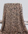 A draped length of rayon challis fabric showcasing its fluid, soft drape as it hangs over a stand. The fabric features a classic black-on-tan leopard print, and the folds highlight the lightweight, matte quality of the material.