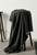 A piece of premium charcoal cotton spandex denim with a frayed edge, elegantly draped over a wooden stool in a minimalist studio setting.