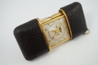 A nice vintage Movado Ermeto Calendar purse watch in gold plated and black leather, crafted during the 1950s. Softly rounded rectangular case measures 50mm while closed, covered by black exotic leather of which shows pulling from edges. Opening and closing is conducted by a winding track, revealing a beautiful white dial with gold dauphine and Arabic hour markers, dauphine hands with lume, gold outer beaded minute track, black inner full calendar track, and day, date and calendar aperture. Fits nicely in the hand, the winding track opens and closes smoothly. The case back contains a lever to prop up the watch on a nightstand or for decor.