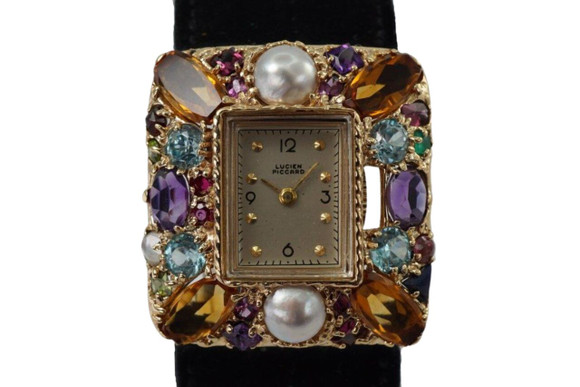 A fine vintage Lucien Piccard watch in 14k yellow gold from the 1960s. Charmingly regarded as “Tutti Frutti” for the ornately adorned 30 mm case of pearls, garnets, amethysts, moonstones, topazes, and sapphires. Features a rectangular silvered dial with black Arabic and round raised gold hour indices, black outer minute track, and gold sword-shaped hands. This piece is accompanied by its original black suede strap and buckle with honeycomb perforations. The crown sits in-between bezel and outer case as to not take away from its overall design, its 10 mm thick profile and cladded multicolor gem stone display will certainly attract attention to wearer’s wrist.