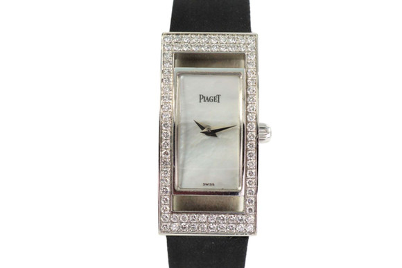 A fine preowned Piaget Limelight reference 54025 in 18k white gold, crafted during the 2000s. Rectangular bezel outfitted with factory set diamonds and open slots on either side of dial, accented with a diamond crown and a white mother of pearl with silver dauphine hands. Paired with a black silk strap, double open closure buckle adorned with diamonds for easy fastening and comfort. A minimal accessory for the wrist with added sparkle, suiting casual and dressy occasions.