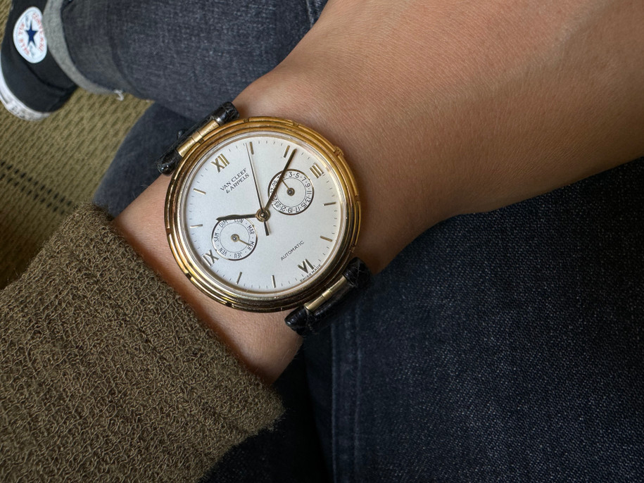 A fine Van Cleef & Arpels Day Date from the LA Collection in 18k yellow gold, crafted during the 2000s. The bezel has detailed grooves and bezeled edges with a small notched crown with VCA logo, the same logo engraved on the case back. Features a white dial with gold accents in the French day and date subsidiary dials, stick hours and Roman numeral indices at 12, 3, 6, and 9 o’clock and sword-shaped hands. VCA black crocodile strap is attached to t-bar lugs with gold plated buckle. The 36 mm case houses an automatic LeCoultre movement, its 9 mm thick profile lends to a substantial presence on the wrist. Great accessory with a classic look for a variety of occasions.