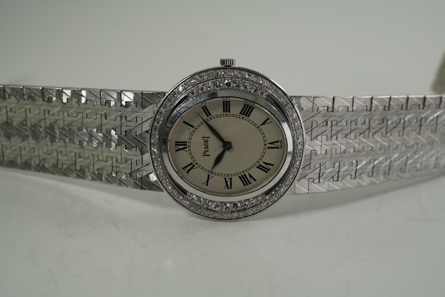 A fine vintage Piaget diamond bracelet watch in 18k white gold, crafted during the 1970s. Featuring a stunning double row of factory set diamonds bezel surrounding a sunburst guilloche dial, blued-steel  leaf-shaped hands and black Roman numeral hour markers and inner minute track. The faceted chevron-style white gold bracelet catches the light dazzlingly, suitable for casual or formalwear. 

Dial has spotting, buckle shows tarnish.
Sapphire crystal.
Piaget cal. 9P, 18 jewels mechanical wind.
Case# 913xx Movement#6379xx
Piaget 18k white gold bracelet, fits 7 1/2 inches approximate.
Buckle signed Piaget Model Depose.
18mm lug width.
Modeled on 6 inch wrist.