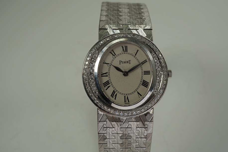 A fine vintage Piaget diamond bracelet watch in 18k white gold, crafted during the 1970s. Featuring a stunning double row of factory set diamonds bezel surrounding a sunburst guilloche dial, blued-steel  leaf-shaped hands and black Roman numeral hour markers and inner minute track. The faceted chevron-style white gold bracelet catches the light dazzlingly, suitable for casual or formalwear. 

Dial has spotting, buckle shows tarnish.
Sapphire crystal.
Piaget cal. 9P, 18 jewels mechanical wind.
Case# 913xx Movement#6379xx
Piaget 18k white gold bracelet, fits 7 1/2 inches approximate.
Buckle signed Piaget Model Depose.
18mm lug width.
Modeled on 6 inch wrist.