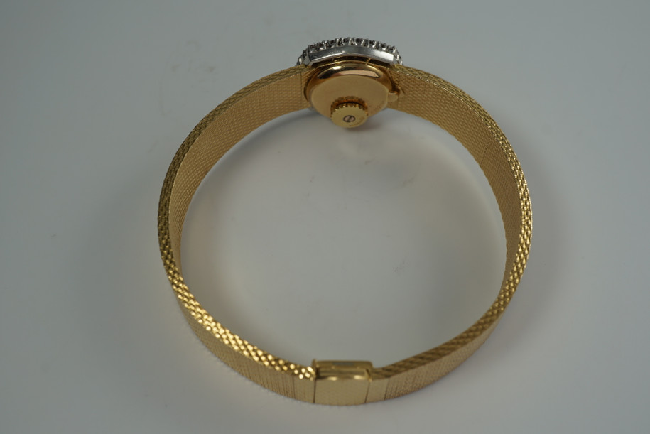A very nice vintage Movado bracelet watch in 18k yellow gold, crafted during the late 1960s. Once retailed by Cartier, the subtle hexagonal polished case with original finish is surrounded by 28 diamonds weighing 1.12 carat total weight, houses a silver dial signed Cartier with black stick and Roman numerals and stick hands. Resembling a floral design further accentuated by a beautifully crafted integrated bracelet with a backwind function that adds to its daintiness. Suitable for casual and dressy occasions.