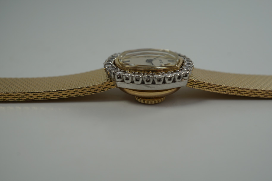 A very nice vintage Movado bracelet watch in 18k yellow gold, crafted during the late 1960s. Once retailed by Cartier, the subtle hexagonal polished case with original finish is surrounded by 28 diamonds weighing 1.12 carat total weight, houses a silver dial signed Cartier with black stick and Roman numerals and stick hands. Resembling a floral design further accentuated by a beautifully crafted integrated bracelet with a backwind function that adds to its daintiness. Suitable for casual and dressy occasions.