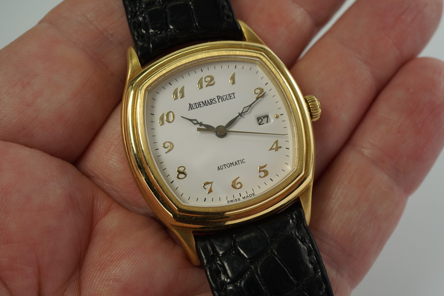 A fine Audemars Piguet “John Schaeffer” automatic watch reference 150101BA.00 in 18k yellow gold from the mid 1990s (as denoted by the D series). Elegant brushed cushion case in original finish with equally elegant white dial with gold Arabic hour indices and black minute hashes, black cathedral hands accented with a gold second hand, and a date aperture at 3 o’clock topped with a gold bead. Slightly curved lugs on a 8.5 mm thick profile would suit a man or woman’s wrist for casual occasions.
Brushed case with original finish.

Sapphire crystal. 

Audemars Piguet 18k buckle.

AP 20mm black alligator strap (70% condition).

Audemars Piguet cal. 2140, 31 jewel movement automatic wind.