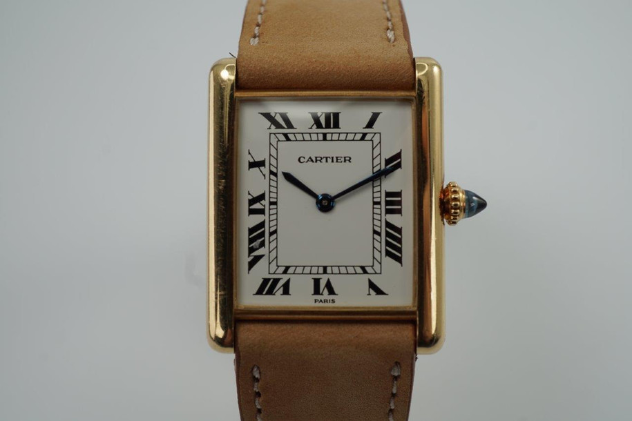 BRAND:                            Cartier 
MODEL:                            Tank
CASE MATERIAL:            18k yellow gold 
CASE MEASURES:          24 x 30 mm
MOVEMENT:                     Mechanical winding
FUNCTIONS:                    Time 
CONDITION:                     Very good
See it in our eBay store.
A beautiful vintage Cartier Tank L.C. in 18k yellow gold, crafted during the 1980s. A special and more refined version of the Tanks, with the extra flat profile, elongated sapphire crown and Paris dial. Would suit a varied wardrobe for an elegant or casual look. Modeled on size 6 inch wrist. 

Tarnishing on case, slight scratches.
Original white Roman dial signed PARIS.
Original blued hands and elongated sapphire crown. 
Case measures 24 x 30 mm, 5 mm thick. 
Cartier cal. 8061 (96), 18 jewels mechanical winding, adjusted to 5 positions. 
Original Cartier 18k deployment with black Must Cartier lizard strap, circumference measures
We will include a non-Cartier leather strap with non-Cartier buckle.
18 mm between lugs.