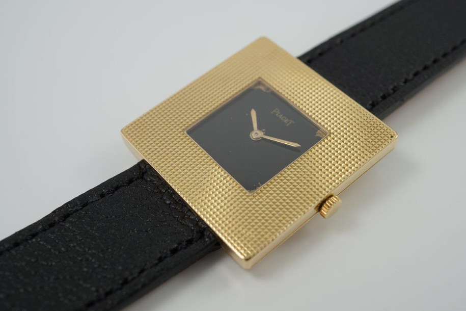 BRAND:                           Piaget
MODEL:                           Square
CASE MATERIAL:            18k yellow gold
CASE MEASURES:          28 mm
MOVEMENT:                     Mechanical winding
FUNCTIONS:                    Time
CONDITION:                     Fine
See it in our eBay store.

A fine rare vintage Piaget square reference 99014 in 18k yellow gold, crafted during the 1970s. At first glance, a minimal piece with its thin profile and black and gold configuration. More meets the eye, however, with the attractive hobnail bezel that softens the bold square frame, and harmoniously symmetrical in scale to the face. Suitable for casual and dressy occasions. Modeled on a 6 inch wrist. 

Light scratches, dial’s corners show underlying gold finish. 
Original black dial, hands and crown. 
Square face measures 14 mm.
Case measures 28 mm, 4.3 mm thick. 
Piaget cal. 9PZ, 18 jewels mechanical winding.
Serial# 2754xx Movement# 768476
Sapphire crystal.
Premium new non-Piaget black leather strap.
Piaget 18k gold buckle.
17 mm between lugs.