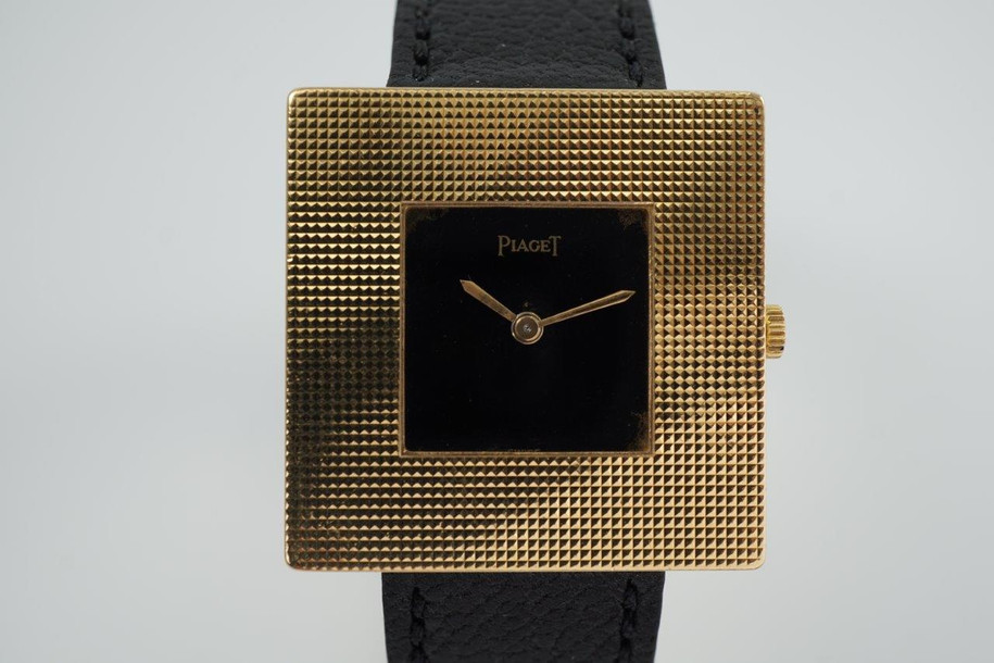 BRAND:                           Piaget
MODEL:                           Square
CASE MATERIAL:            18k yellow gold
CASE MEASURES:          28 mm
MOVEMENT:                     Mechanical winding
FUNCTIONS:                    Time
CONDITION:                     Fine
See it in our eBay store.

A fine rare vintage Piaget square reference 99014 in 18k yellow gold, crafted during the 1970s. At first glance, a minimal piece with its thin profile and black and gold configuration. More meets the eye, however, with the attractive hobnail bezel that softens the bold square frame, and harmoniously symmetrical in scale to the face. Suitable for casual and dressy occasions. Modeled on a 6 inch wrist. 

Light scratches, dial’s corners show underlying gold finish. 
Original black dial, hands and crown. 
Square face measures 14 mm.
Case measures 28 mm, 4.3 mm thick. 
Piaget cal. 9PZ, 18 jewels mechanical winding.
Serial# 2754xx Movement# 768476
Sapphire crystal.
Premium new non-Piaget black leather strap.
Piaget 18k gold buckle.
17 mm between lugs.