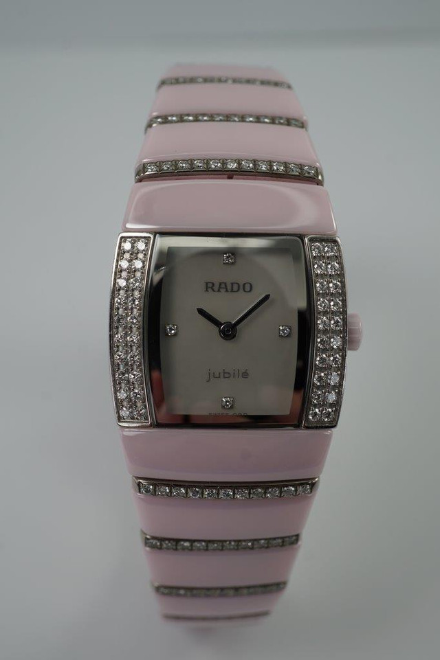 BRAND:                          Rado
MODEL:                          Sintra Jubile 
CASE MATERIAL:           Ceramic and diamond
CASE MEASURES:          22 x 27 mm
MOVEMENT:                   Quartz  
FUNCTIONS:                   Time
CONDITION:                    Fine
See it in our eBay store.

A very nice preowned Rado Sintra Jubilee in ceramic, crafted during the 2010s. A sweet little watch for the wearer who enjoys wearing a delicate pink watch with accented diamond bezel and bracelet, featuring a mother of pearl dial and diamond hour markers. Wears comfortably with its size and weight, and double-fold clasp. The crown is in the shape of a flower that makes this piece extra special. Modeled on size 6 inch wrist.

Minimal scratches. 
Factory diamond bezel, mop diamond dial and 8 rows of graduating diamonds. 
Case measures 22 x 27 mm, 7.5mm thick.
Rado quartz movement.
Serial# 1D118056
Sapphire crystal.
Rado bracelet fits 6 1/2 inches.
18mm graduated bracelet.
Last known retail: 5,600 USD.