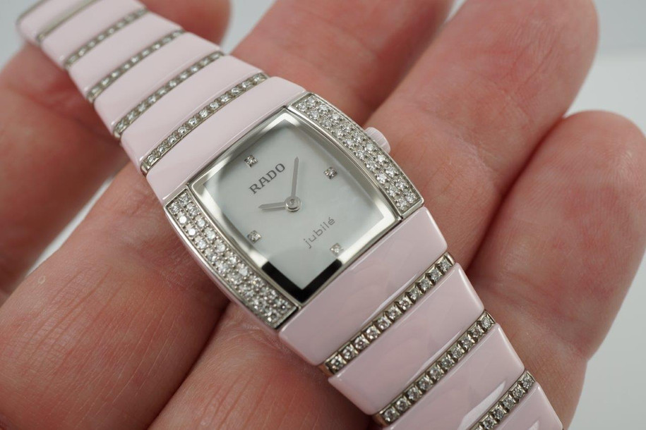 BRAND:                          Rado
MODEL:                          Sintra Jubile 
CASE MATERIAL:           Ceramic and diamond
CASE MEASURES:          22 x 27 mm
MOVEMENT:                   Quartz  
FUNCTIONS:                   Time
CONDITION:                    Fine
See it in our eBay store.

A very nice preowned Rado Sintra Jubilee in ceramic, crafted during the 2010s. A sweet little watch for the wearer who enjoys wearing a delicate pink watch with accented diamond bezel and bracelet, featuring a mother of pearl dial and diamond hour markers. Wears comfortably with its size and weight, and double-fold clasp. The crown is in the shape of a flower that makes this piece extra special. Modeled on size 6 inch wrist.

Minimal scratches. 
Factory diamond bezel, mop diamond dial and 8 rows of graduating diamonds. 
Case measures 22 x 27 mm, 7.5mm thick.
Rado quartz movement.
Serial# 1D118056
Sapphire crystal.
Rado bracelet fits 6 1/2 inches.
18mm graduated bracelet.
Last known retail: 5,600 USD.