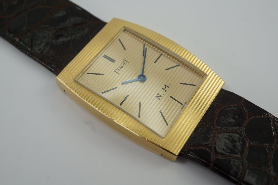 BRAND:                          Piaget
MODEL:                          Retailed by N.M.
CASE MATERIAL:           18k yellow gold
CASE MEASURES:          25 x 31.5 mm
MOVEMENT:                   Mechanical
FUNCTIONS:                   Time
CONDITION:                    Fine
See it in our eBay store.

A fine Piaget reference 9672 reference 9672, crafted circa 1970-80. An unusual and gorgeous tonneau-shaped Piaget accessory originally retailed by Neiman Marcus, featuring horizontal fluting spanning across dial and case, with initials N.M. Tonal gold lends to an eye-catching quality with reflective blue hands and matte black stick indexes. Great addition to collectors repertoire, accompanied by the original leather strap and Piaget signed buckle. Modeled on 6 inch wrist.

Unpolished, original finish. 
Vivid hallmarks: hand inscribed Neiman Marcus inventory number 7094 located by crown.
Original dial, hands and crown. 
Case measures 25 x 31.5 mm, 5 thick.
Piaget cal., 9P, 18 jewels mechanical winding.  
Serial# 1115xx
Sapphire crystal.
Piaget brown crocodile strap (90% condition approximate), original to model.
Piaget signed 18k gold buckle. 
19mm between lugs.
