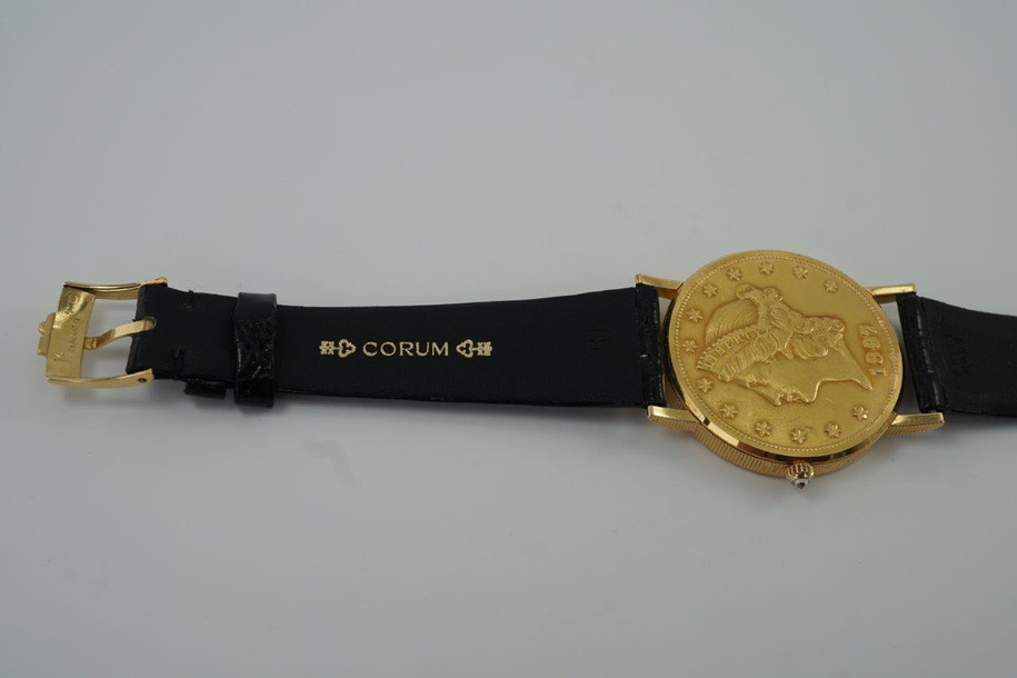 A fine Corum 20 Dollar Coin watch in 18k yellow gold, crafted during the 1990s. USA coin from 1897 exhibits little wear, with the classic ridged coin case and diamond crown. Durable for everyday wear, features a date aperture and black hands contrasting delightfully against the gold face, paired with a glossy alligator black strap. Modeled on 6 inch wrist.

Box included.
Original dial, hands and crown. 
Case measures 36 x 42 mm, 6 mm thick. 
Corum quartz, 10 jewels 
Case# 3763xx Movement# 2194xx
Sapphire crystal. 
Corum black alligator strap, unused.
Corum plated buckle. 
20mm lug width.