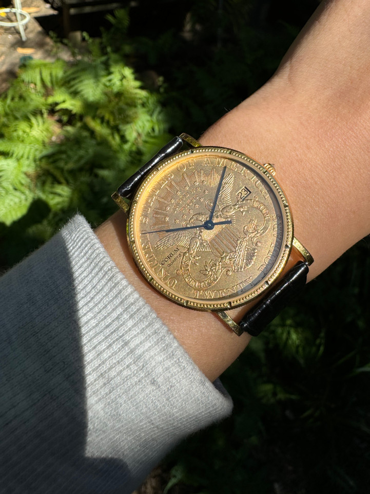 A fine Corum 20 Dollar Coin watch in 18k yellow gold, crafted during the 1990s. USA coin from 1897 exhibits little wear, with the classic ridged coin case and diamond crown. Durable for everyday wear, features a date aperture and black hands contrasting delightfully against the gold face, paired with a glossy alligator black strap. Modeled on 6 inch wrist.

Box included.
Original dial, hands and crown. 
Case measures 36 x 42 mm, 6 mm thick. 
Corum quartz, 10 jewels 
Case# 3763xx Movement# 2194xx
Sapphire crystal. 
Corum black alligator strap, unused.
Corum plated buckle. 
20mm lug width.