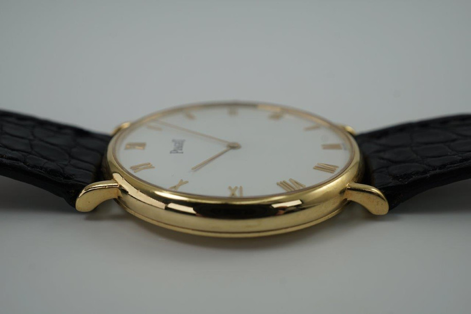 A very nice preowned Piaget watch in 18k yellow gold reference 8035, crafted during the 1990-2000s. A classic configuration of understated gold round smooth case, white dial and gold applied hours and Roman numerals. This piece will take you from executive look to a casual occasion, featuring an ultra-thin profile and paired with a black strap. Suitable for men or women.

Minimal scratches. 
Original dial, hands and crown.
Case measures 32.5 x 35 mm, 4.5mm thick. 
Piaget cal. 858P quartz movement. 
Case# 594500 Movement# 9901021 
Sapphire crystal. 
Piaget black crocodile strap (80% condition approximate).
Piaget 18k gold buckle.
17mm lug width.