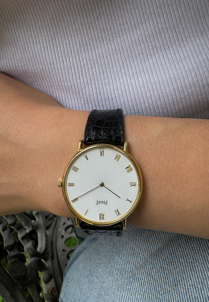 A very nice preowned Piaget watch in 18k yellow gold reference 8035, crafted during the 1990-2000s. A classic configuration of understated gold round smooth case, white dial and gold applied hours and Roman numerals. This piece will take you from executive look to a casual occasion, featuring an ultra-thin profile and paired with a black strap. Suitable for men or women.