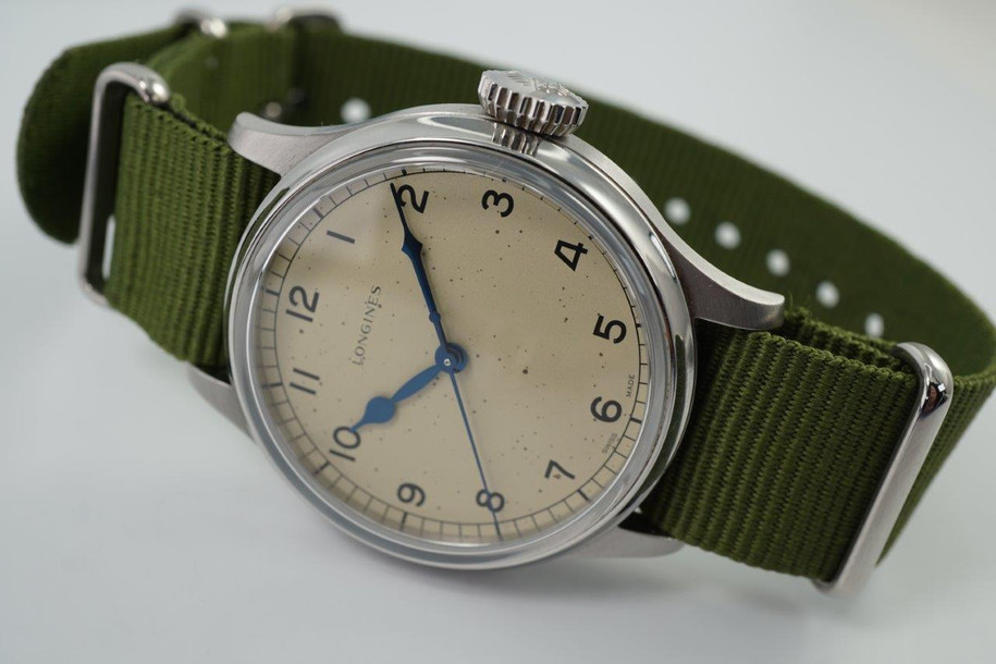 A fine Longines Heritage Military reference L2.819.4.93.2 in stainless steel. A 1940’s reissue of Longines’ enduring association to the realm of aviation brought this model, current in today’s catalogue of the Longines Heritage collection with US. Retail of $2425. Longines describes this dial color as silver, although it appears to be more beige with faint splattering of dots, bearing a patina-like impression of its vintage predecessor. The painted Arabic numerals and railroad ring for the minutes, typical of military pieces of its time. Wears handsomely on the wrist, and may be rotated with a Velle Alexander custom strap or military green nato-style strap, apropos to its theme.  

Original dial, blued steel hands and crown.
Case measures 38.5 x 47.6 mm, 11.70mm thick. 
Longines automatic movement.
Serial# 498242xx
Sapphire crystal.
New generic green 19mm Nato-style strap.
Extra long Velle Alexander custom strap, like new.
Longines 18mm steel signed buckle.
19mm lug width.